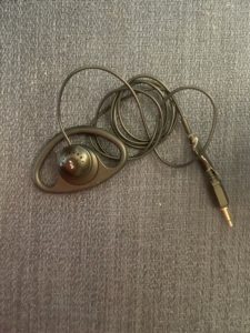 Photo of one ear earpiece- it has an ear loop and a mini-microphone plug. From Annie Chiappetta, 2021